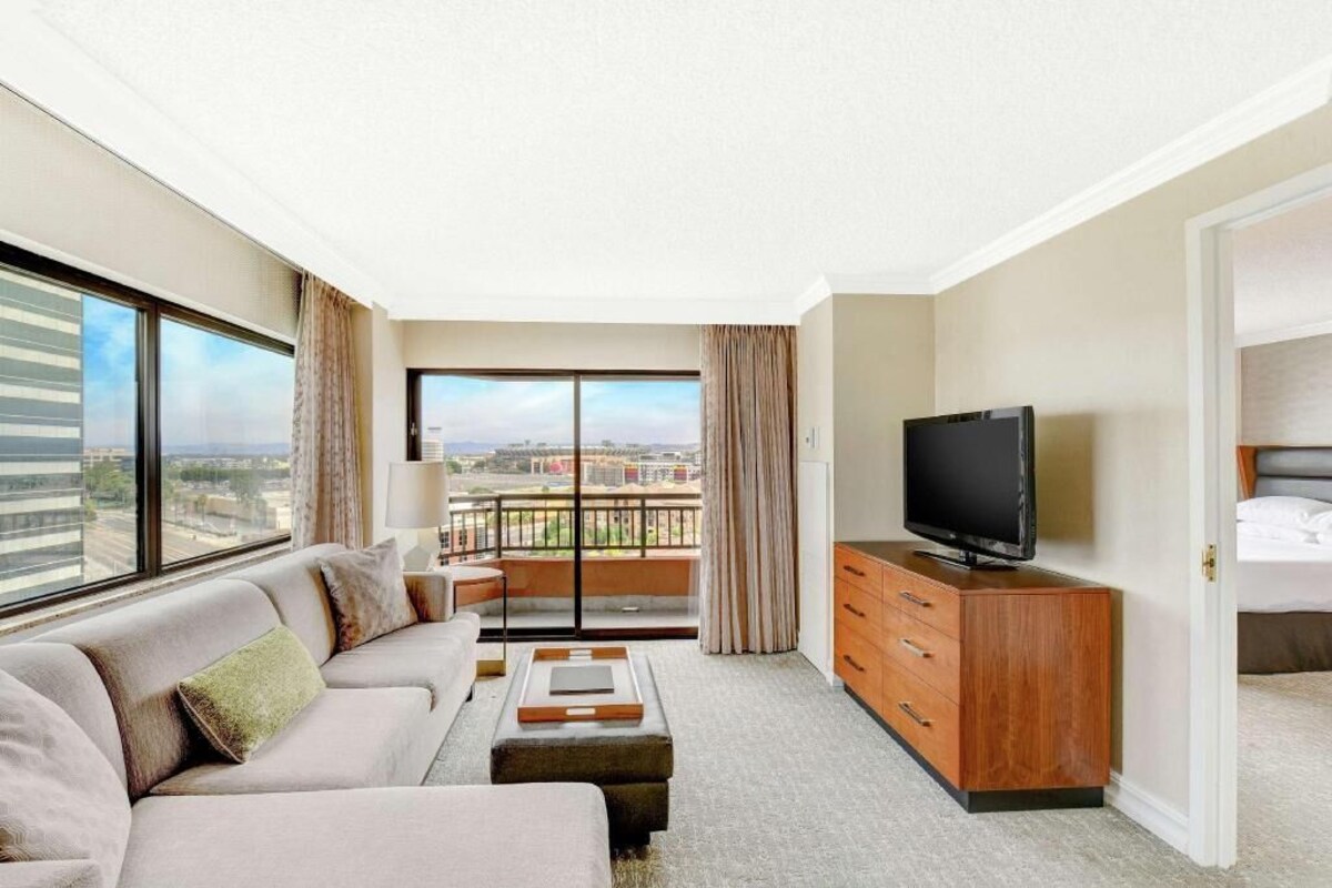 A hotel room with a balcony, a sofa, a TV, and a wooden dresser.