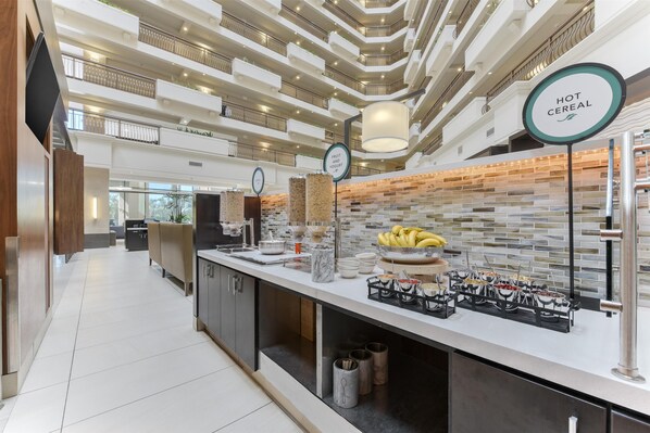A hotel lobby with a modern design, featuring a multi-level atrium, a fruit and yogurt station, and a hot cereal counter.