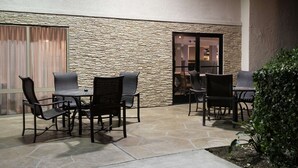 An outdoor patio with stone flooring, a stone wall, and a table with chairs. - Hampton Inn Los Angeles/Santa Clarita (Stevenson Ranch)