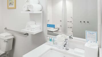 Un baño moderno con inodoro, lavamanos y ducha. Hay toallas en un estante y un cartel sobre la limpieza.