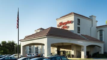 A Hampton Inn hotel with a clear sign, a parking lot, and a flagpole with the American flag.