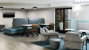A modern lounge area with seating arrangements, a flat-screen TV, and a view of the outdoors. - Hampton Inn Los Angeles/Santa Clarita (Stevenson Ranch)