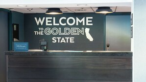 A reception desk with a "Welcome to the Golden State" sign and a "Hilton Honors" badge. - Hampton Inn Los Angeles/Santa Clarita (Stevenson Ranch)
