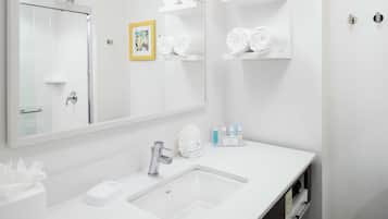 A modern bathroom with a large mirror, a white sink, and shelves with neatly folded towels.