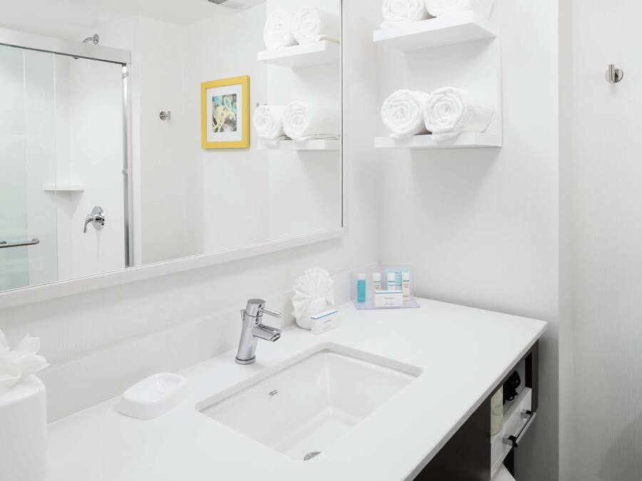 A modern bathroom with a large mirror, a white sink, and shelves with neatly folded towels.