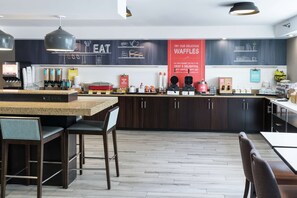 Una cocina moderna con armarios de madera oscura, encimera de granito y una isla central con asientos. Se observan varios electrodomésticos y un menú en una pizarra en la pared.
