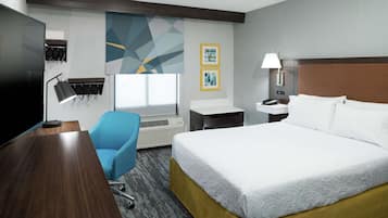 Habitación de hotel con una cama grande, un escritorio, una silla, un televisor, una lámpara y obras de arte en la pared.