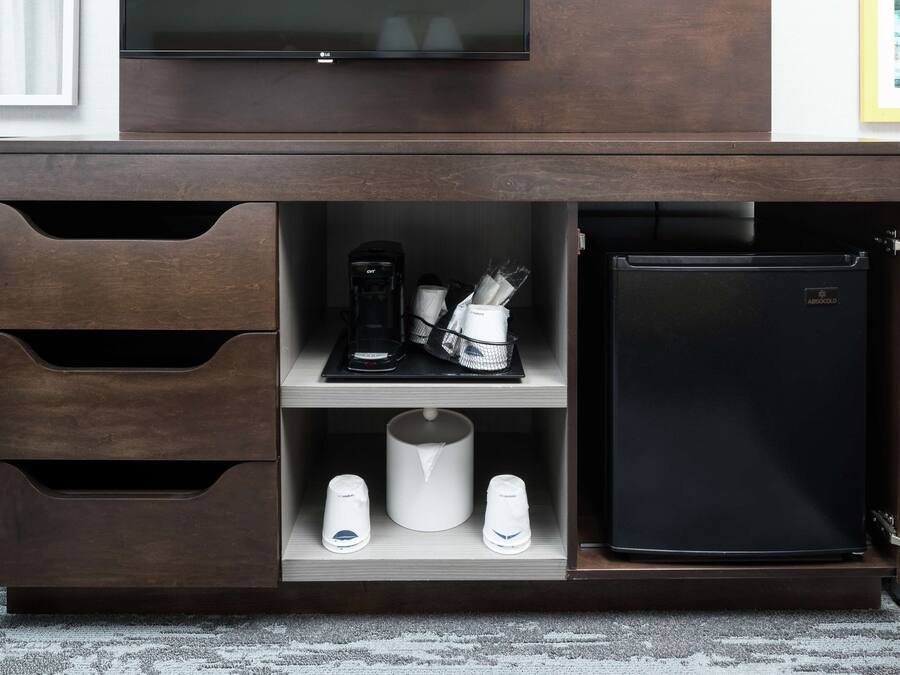Minibar com cafeteira, duas chávenas e um frigorífico preto.