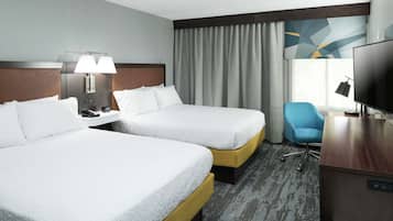 A hotel room with two beds, a desk, a TV, and a chair.