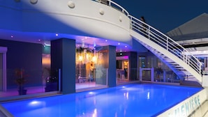 A swimming pool with a staircase and a railing, surrounded by a building with glass walls and indoor seating areas. - Karibea Valmenière Hôtel (Fort-de-France)