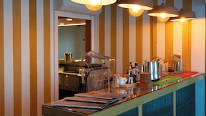 A bar area with striped wallpaper, hanging pendant lights, and a variety of bar tools and bottles on the counter. - Karibea Valmenière Hôtel (Fort-de-France)
