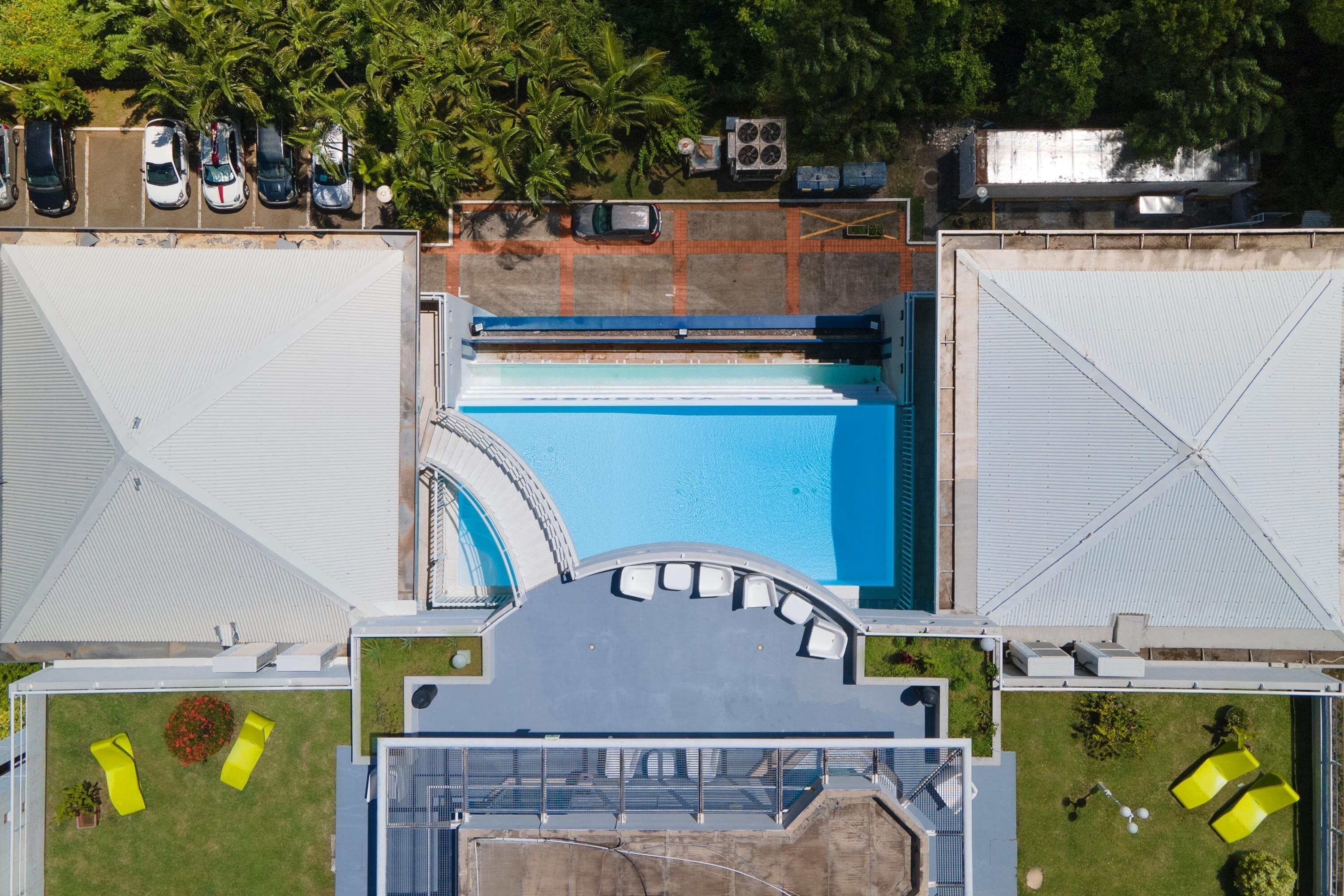 Luftaufnahme eines Hotels mit Schwimmbad, mehreren Parkplätzen und einem überdachten Außenbereich mit Sitzgelegenheiten.