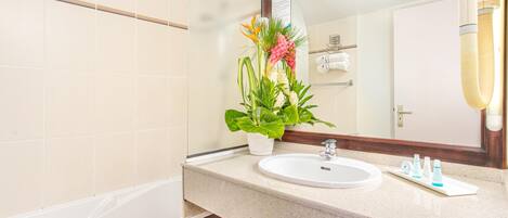Un baño con un lavabo blanco, un espejo y una planta en maceta.