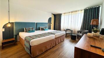 A hotel room with a large bed, a desk, a chair, and a lamp.