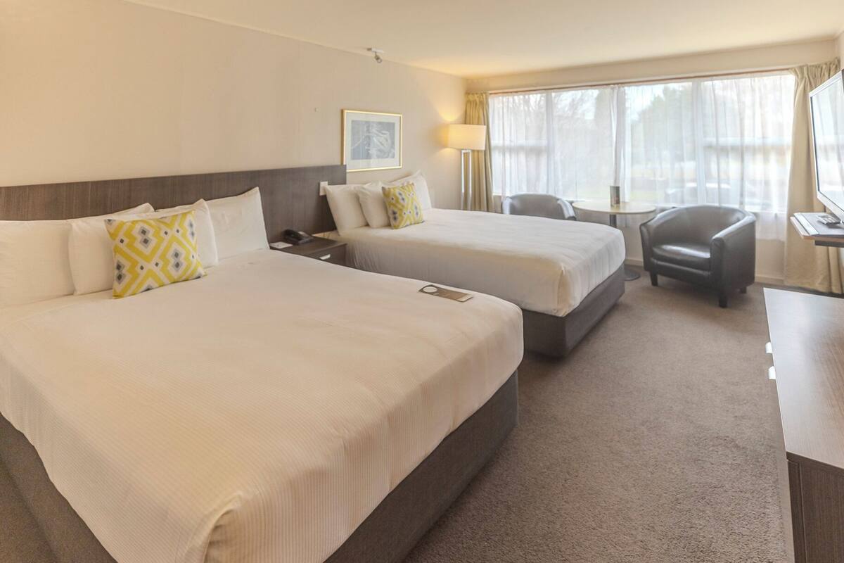 A hotel room with two beds, a desk, a chair, and a lamp.