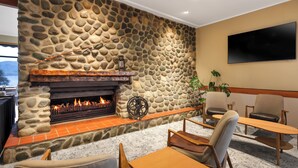 A stone fireplace with a fire, surrounded by seating and a television. - Kingsgate Hotel Te Anau (Te Anau)