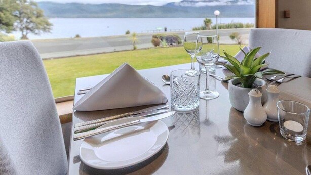 A dining table set with plates, cutlery, and glasses, with a view of a lake and mountains in the background. - Kingsgate Hotel Te Anau (Te Anau)