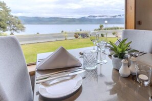 A dining table set with plates, cutlery, and glasses, with a view of a lake and mountains in the background. - Kingsgate Hotel Te Anau (Te Anau)