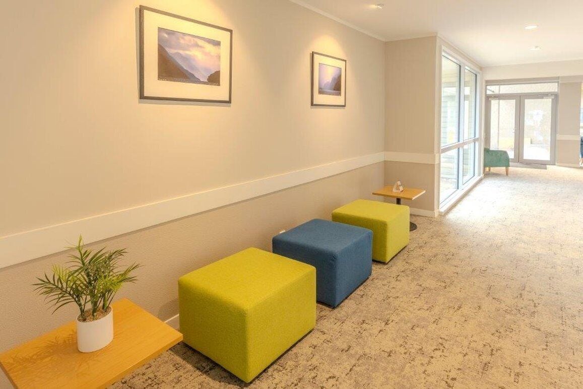 Um corredor com três pufes coloridos, uma pequena mesa com uma planta e quadros nas paredes.