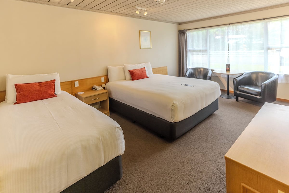A hotel room with two beds, a desk, a chair, and a window with curtains.
