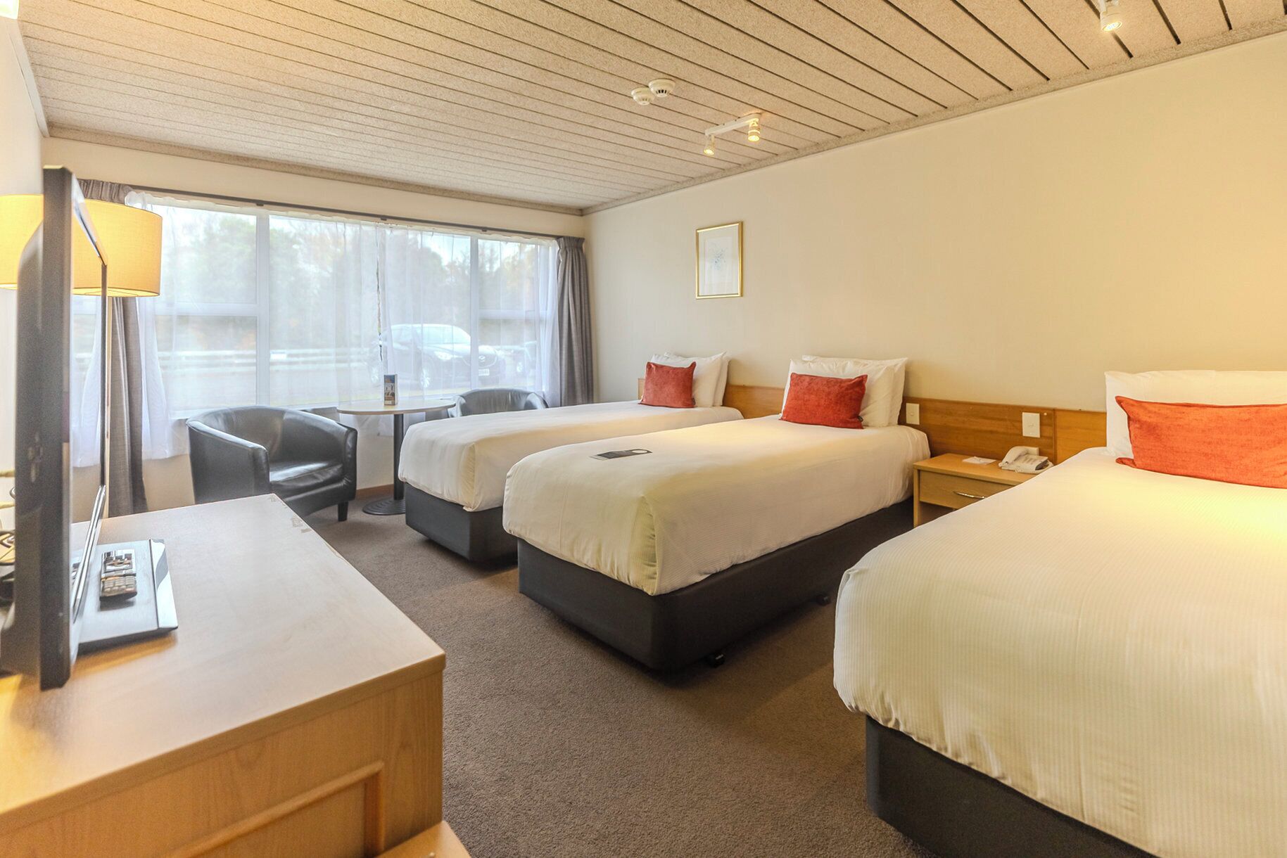 Une chambre d’hôtel avec deux lits, un bureau, une chaise et une fenêtre avec des rideaux.