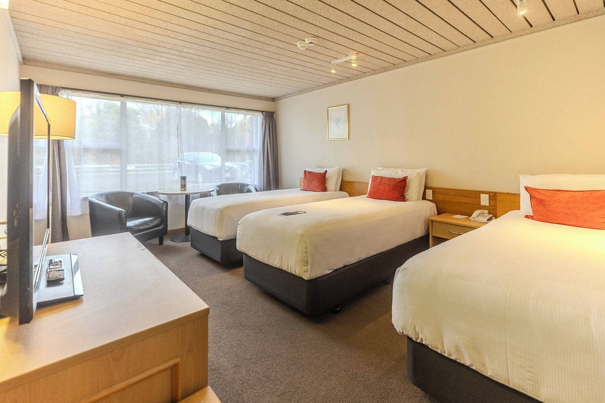 A hotel room with two beds, a desk, a chair, and a window with curtains.