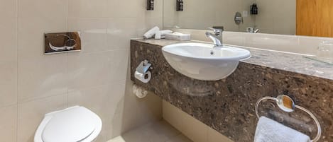 A modern bathroom with a white toilet, a sink with a marble countertop, and a mirror above the sink.