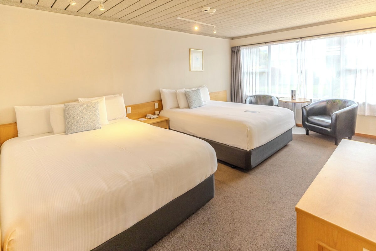 A hotel room with two beds, a desk, a chair, and a window with curtains.