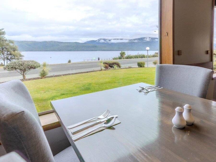 A dining table set with cutlery and salt shakers, overlooking a lake and mountains.