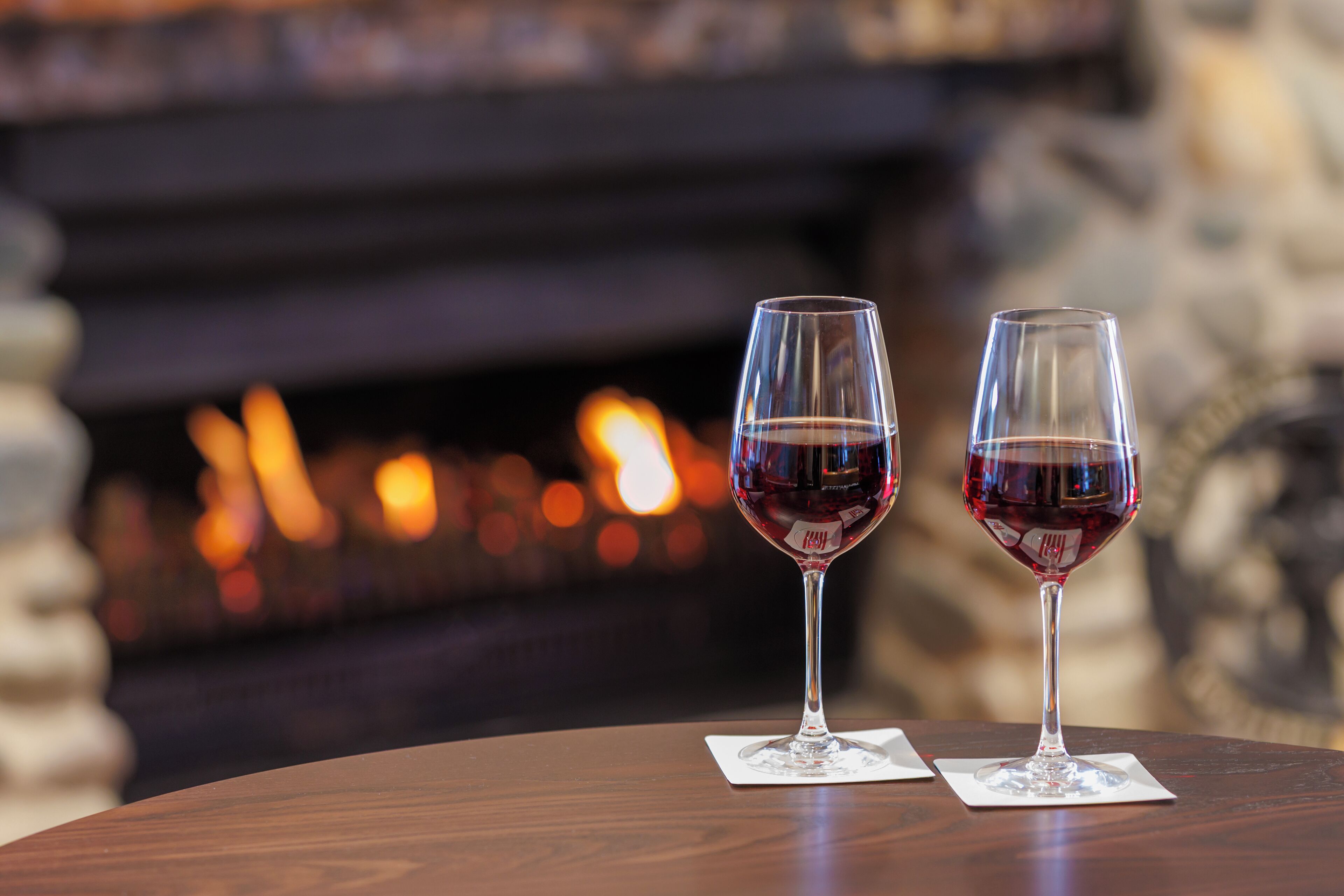 Dos copas de vino sobre una mesa de madera, con una chimenea al fondo.