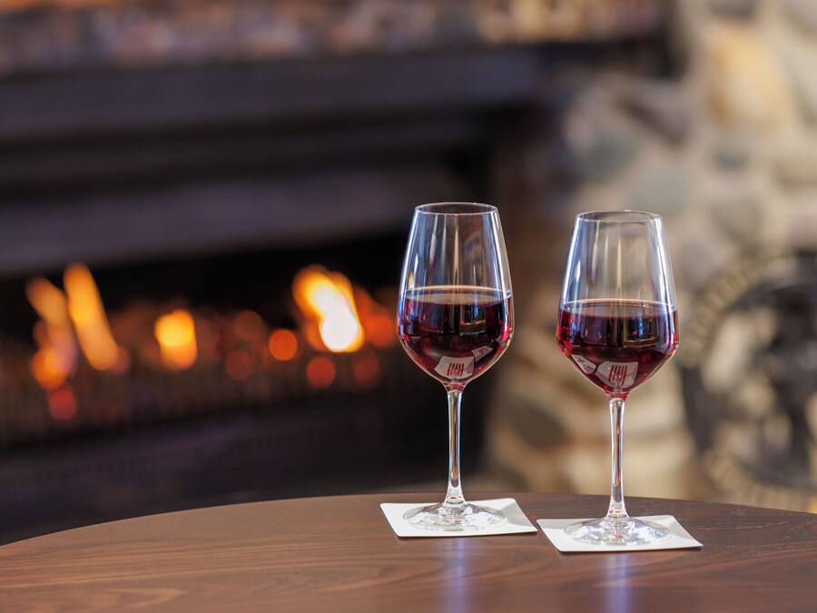 Dos copas de vino sobre una mesa de madera, con una chimenea al fondo.