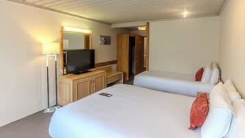 A hotel room with two beds, a TV, a lamp, and a wooden wardrobe.