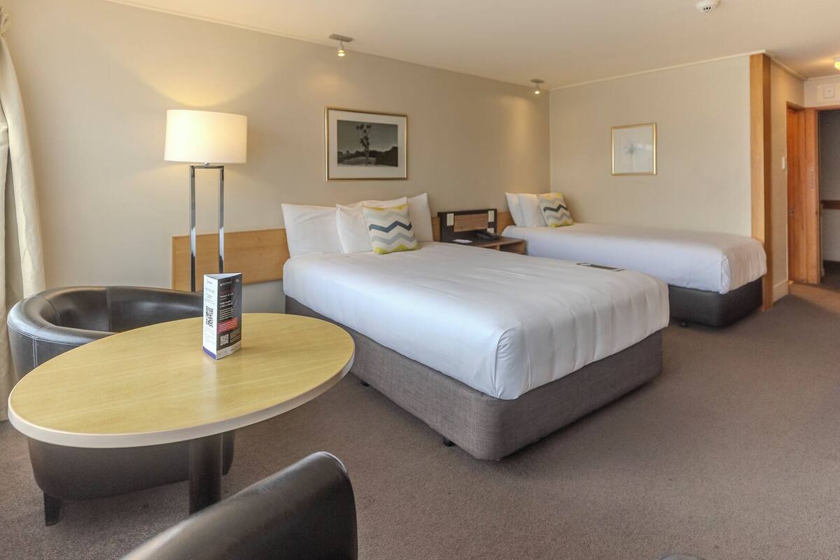 A hotel room with two beds, a round table, a chair, a lamp, and a picture on the wall.