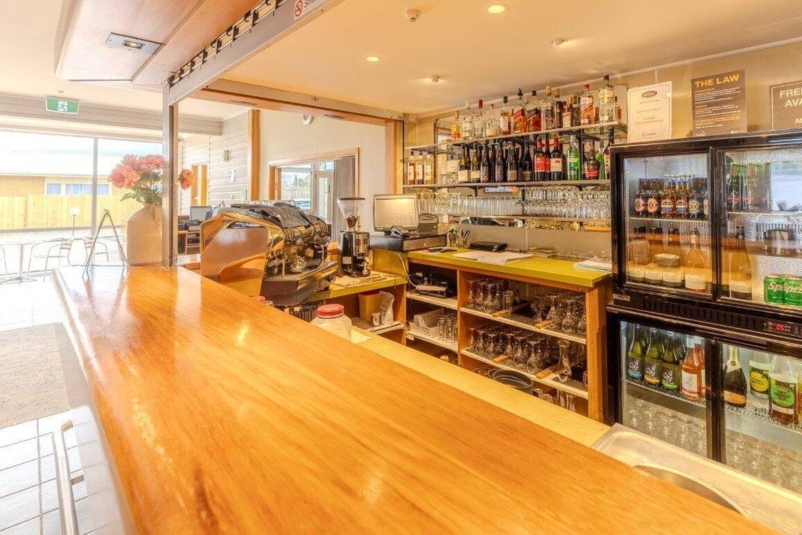 A bar area with a wooden counter, shelves of bottles, and a refrigerator.