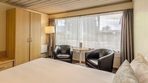 A hotel room with a large bed, two black leather chairs, a small round table, a lamp, and a window with curtains. - Kingsgate Hotel Te Anau (Te Anau)
