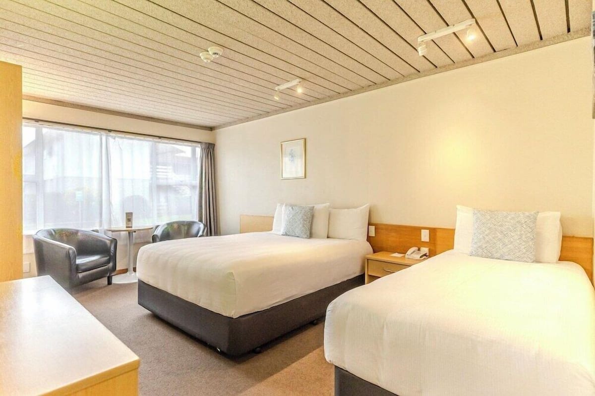 A hotel room with two beds, a desk, a chair, a small table, and a window with curtains.