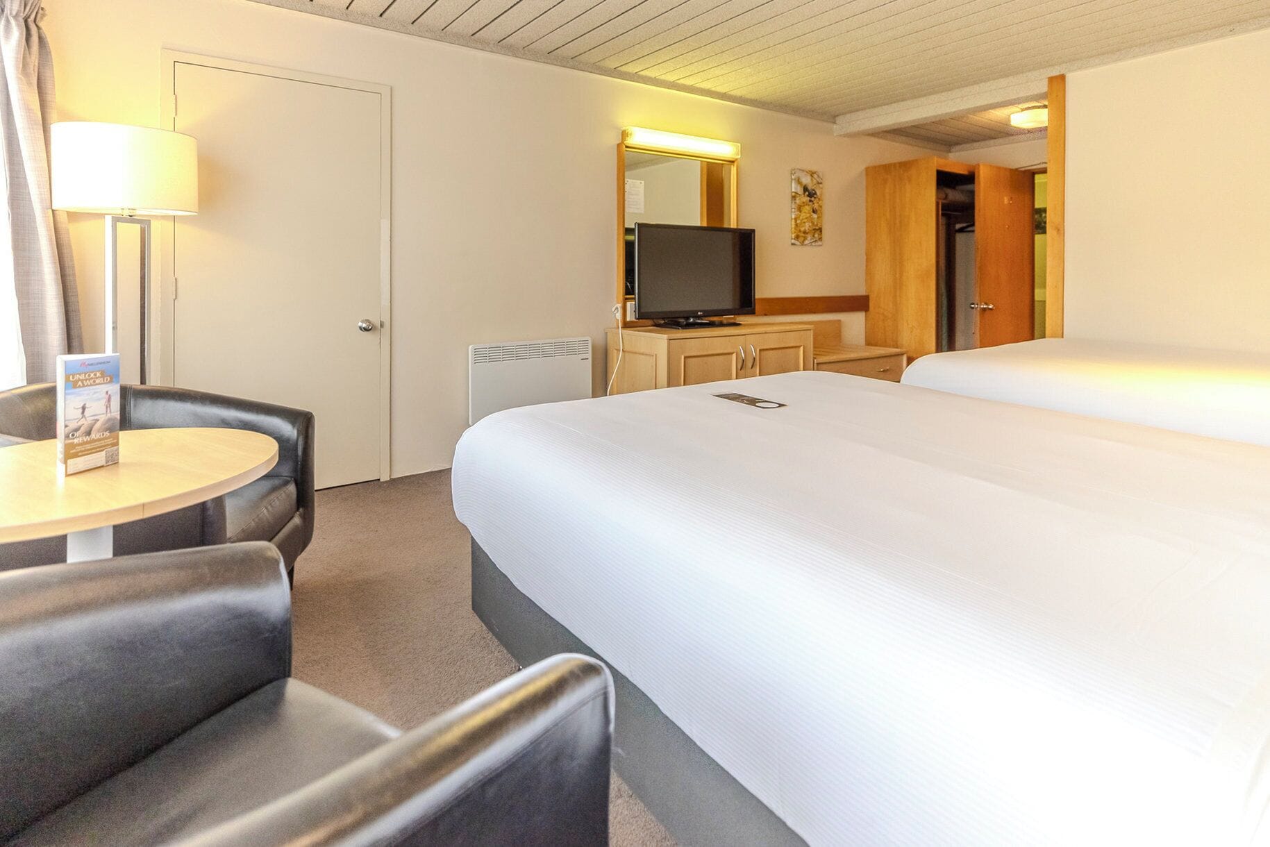 A hotel room with a bed, a desk with a lamp, a television, and a wardrobe.