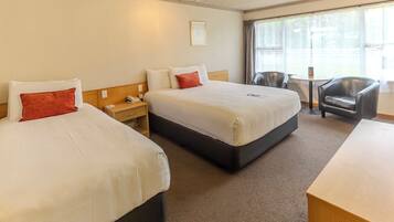 A hotel room with two beds, a desk, a chair, and a window with curtains.