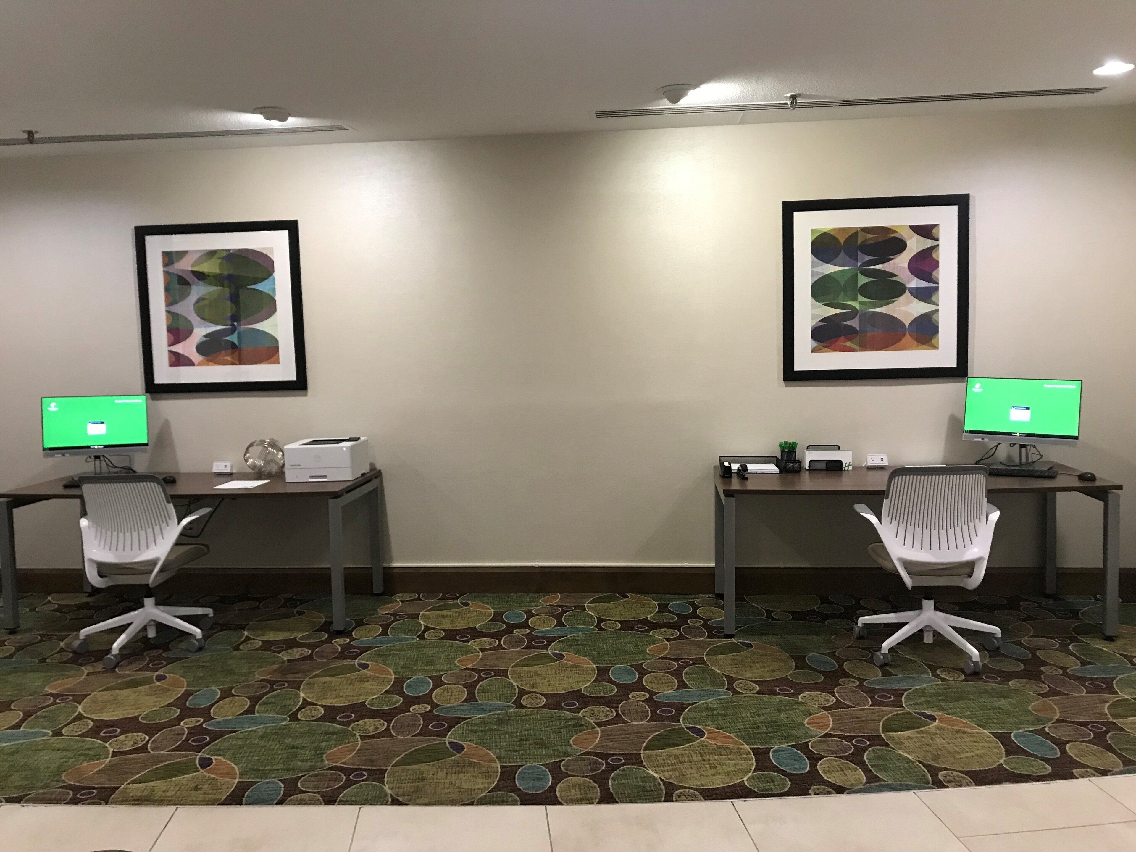 A room with two desks, each with a computer monitor, a printer, and a chair. There are framed artworks on the walls.