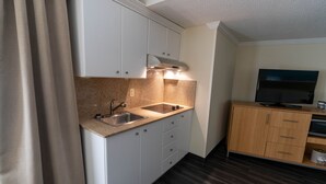 A compact kitchen with white cabinets, a granite countertop, a stainless steel sink, and a built-in range hood. There is a wooden cabinet with a flat-screen TV and a small shelf below it. - Holiday Inn Greenville by IHG (Greenville)