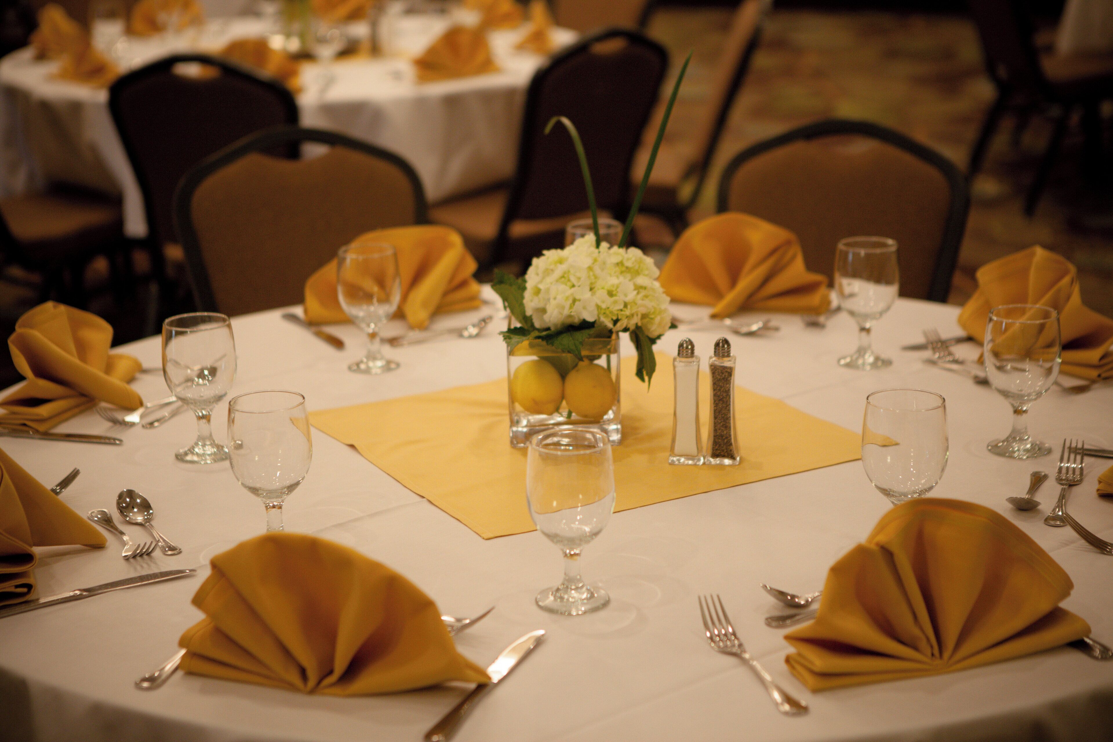 A round dining table set with yellow napkins, wine glasses, and cutlery.