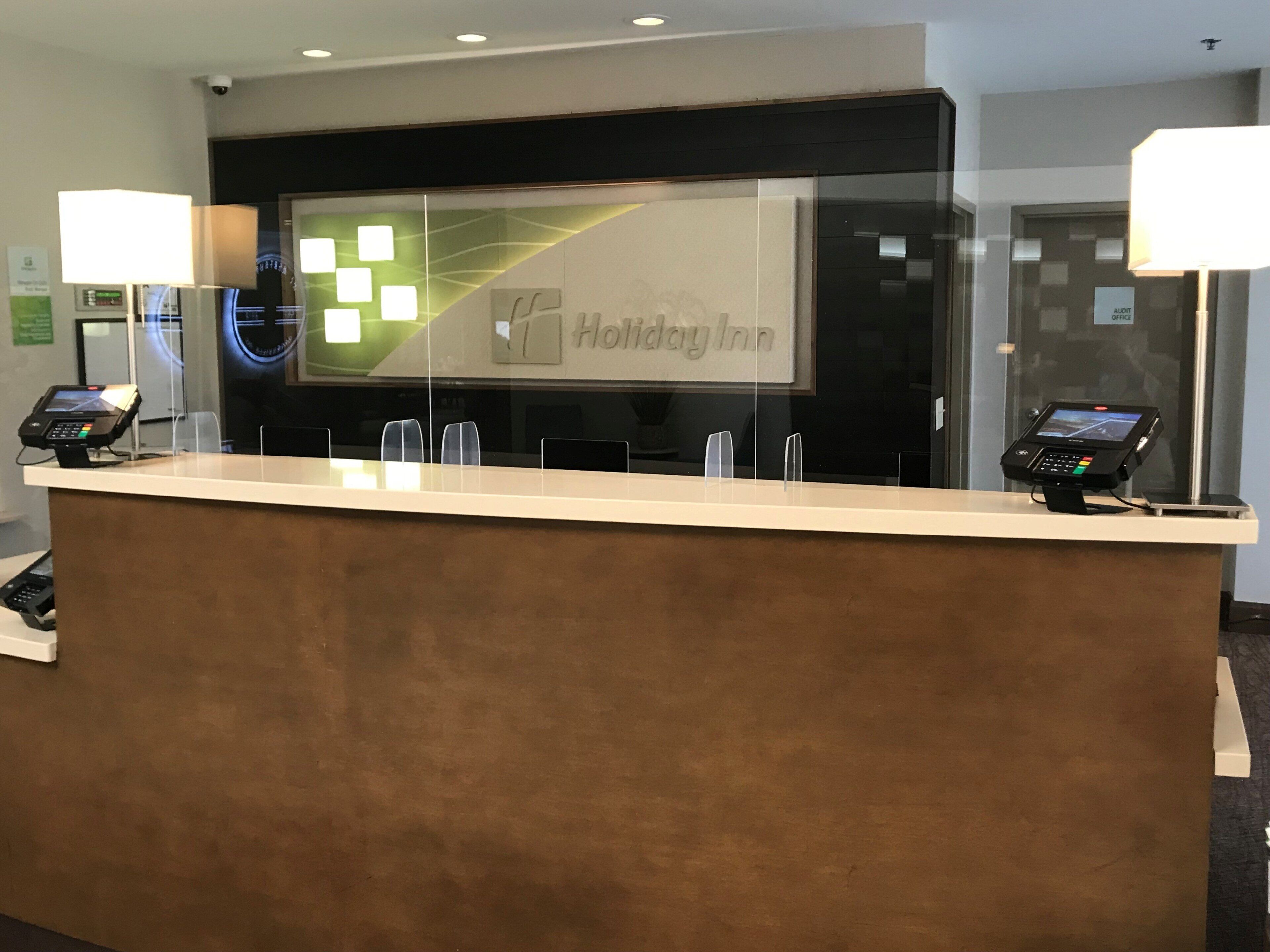 Un comptoir d’accueil d’un hôtel Holiday Inn, doté d’une cloison en verre, de deux téléphones et d’un écran numérique.