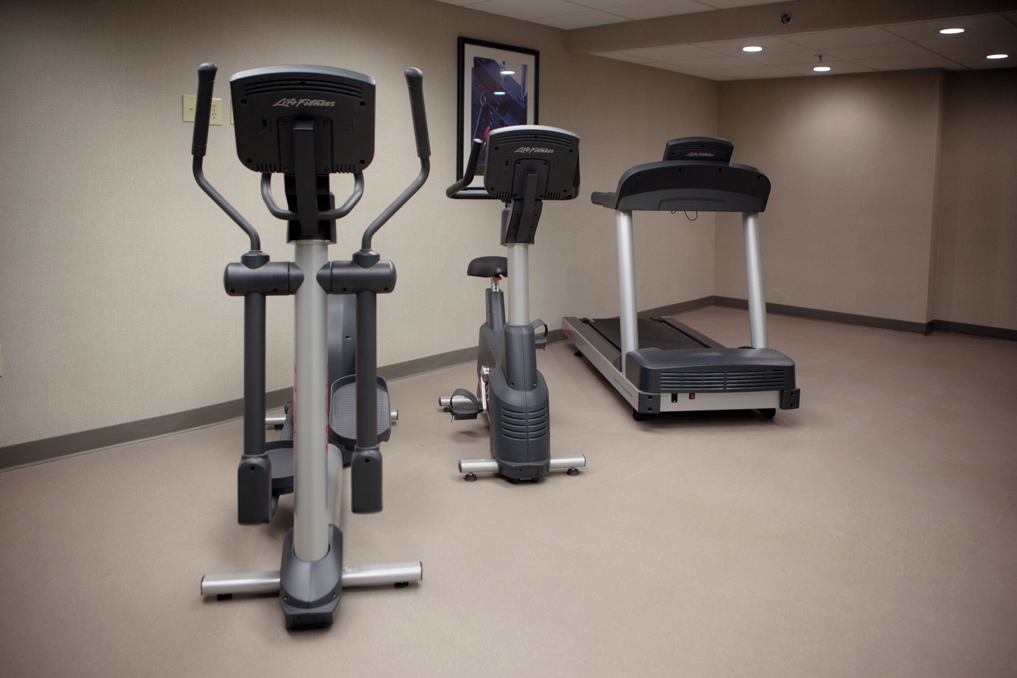 Un espacio de acondicionamiento físico con máquinas de cardio, incluyendo una caminadora y una elíptica.