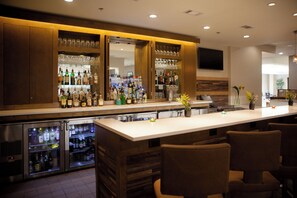 A bar area with a long counter, multiple shelves of bottles, glasses, and a television mounted on the wall. - Holiday Inn Greenville by IHG (Greenville)