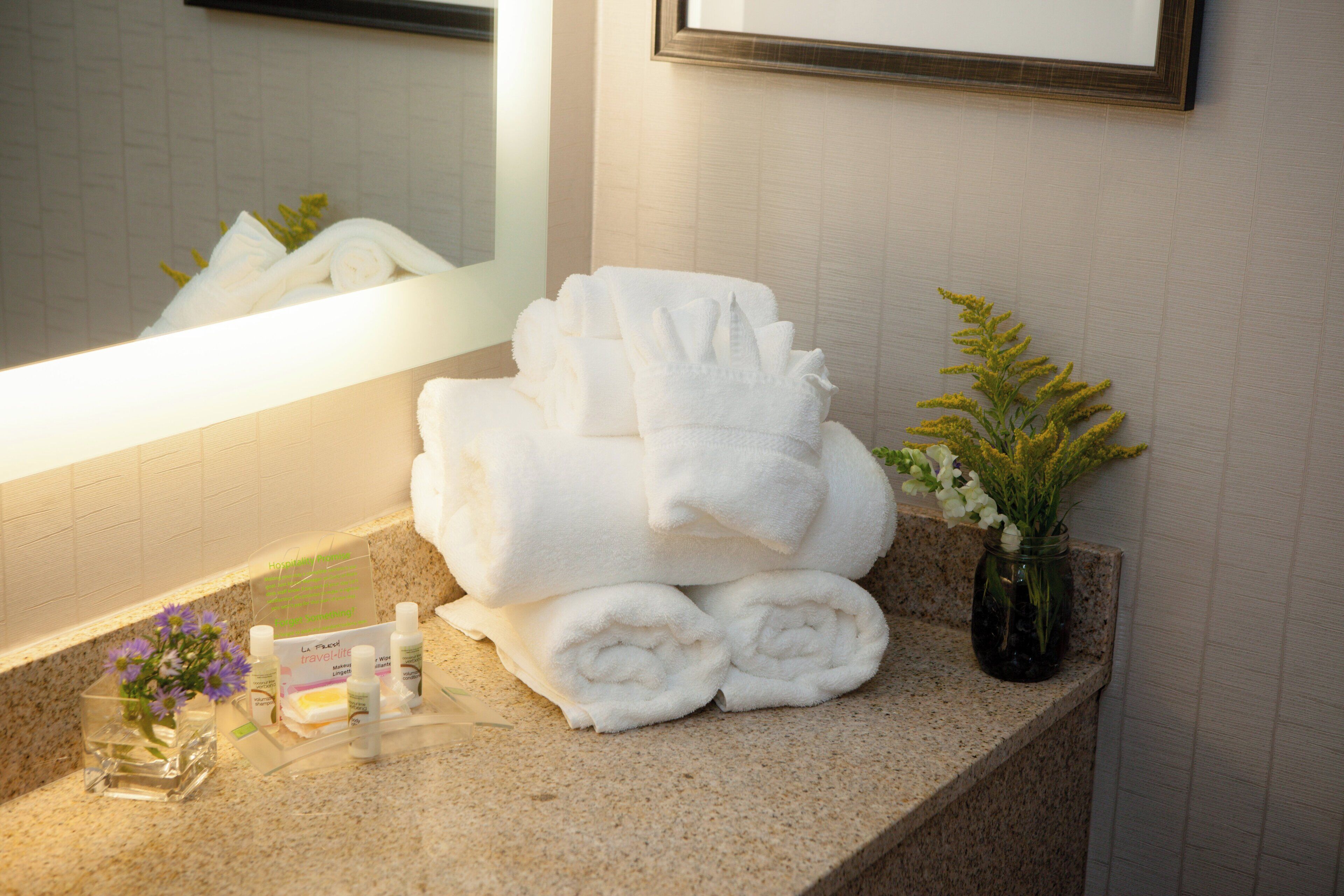 Un meuble-lavabo dans la salle de bain, avec des serviettes blanches soigneusement pliées, un petit vase avec des fleurs et des articles de toilette.