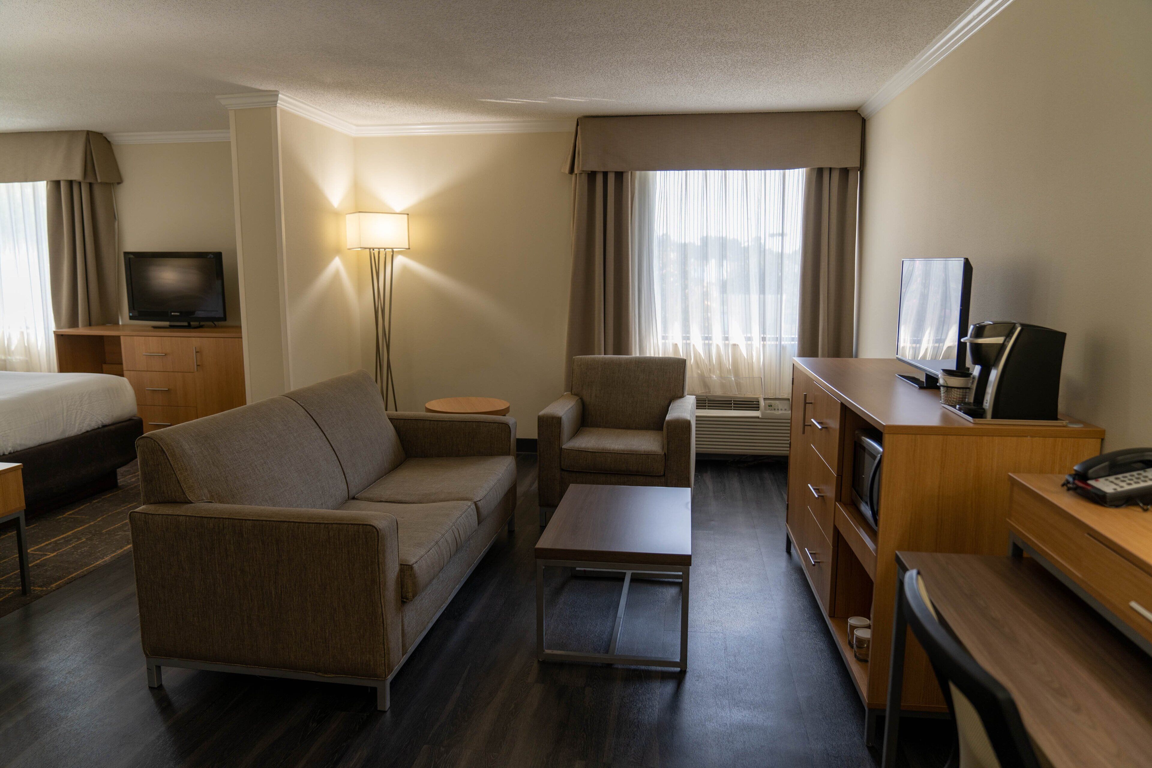A hotel room with a bed, a sofa, a desk, a television, and a lamp.
