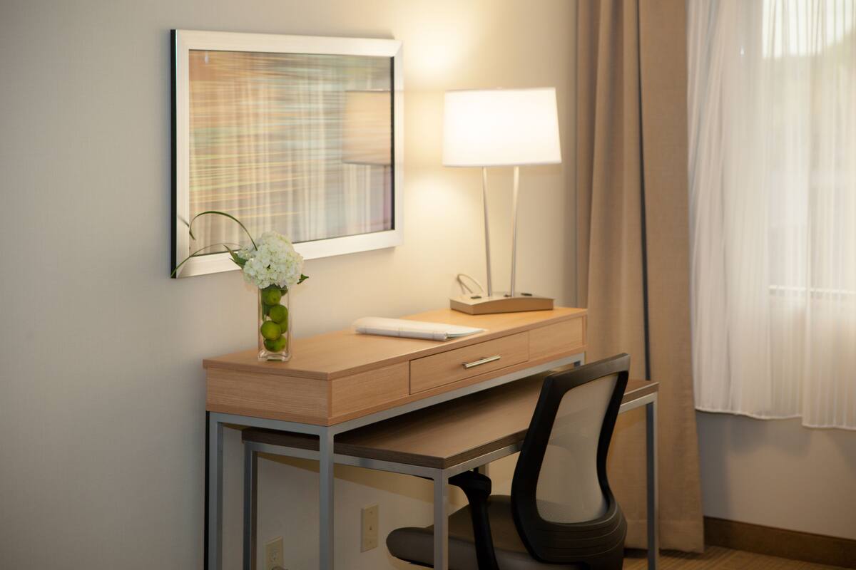 Ein Hotelzimmer mit Schreibtisch, Stuhl, Lampe und einem Bild an der Wand.