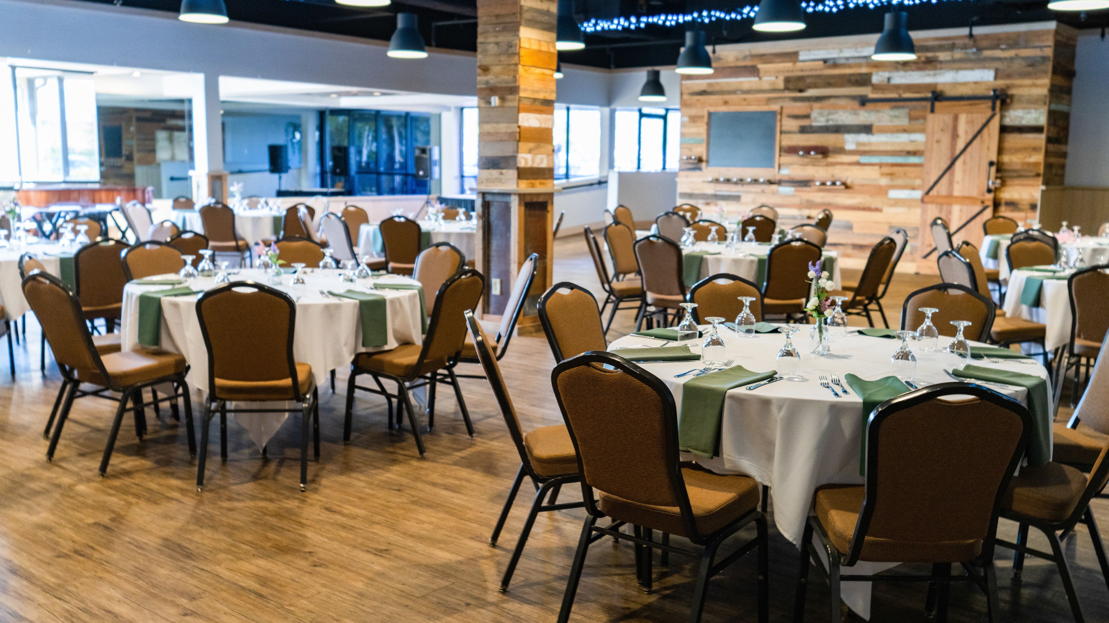 A spacious dining area with multiple round tables, each set with chairs, glasses, and cutlery.