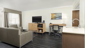 A hotel room with a sofa, a desk with a computer, a TV, a microwave, a coffee maker, a sink, and a painting on the wall. - Holiday Inn Greenville by IHG (Greenville)