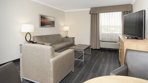 A hotel room with a sofa, a small table, a TV on a cabinet, and a window with curtains. - Holiday Inn Greenville by IHG (Greenville)